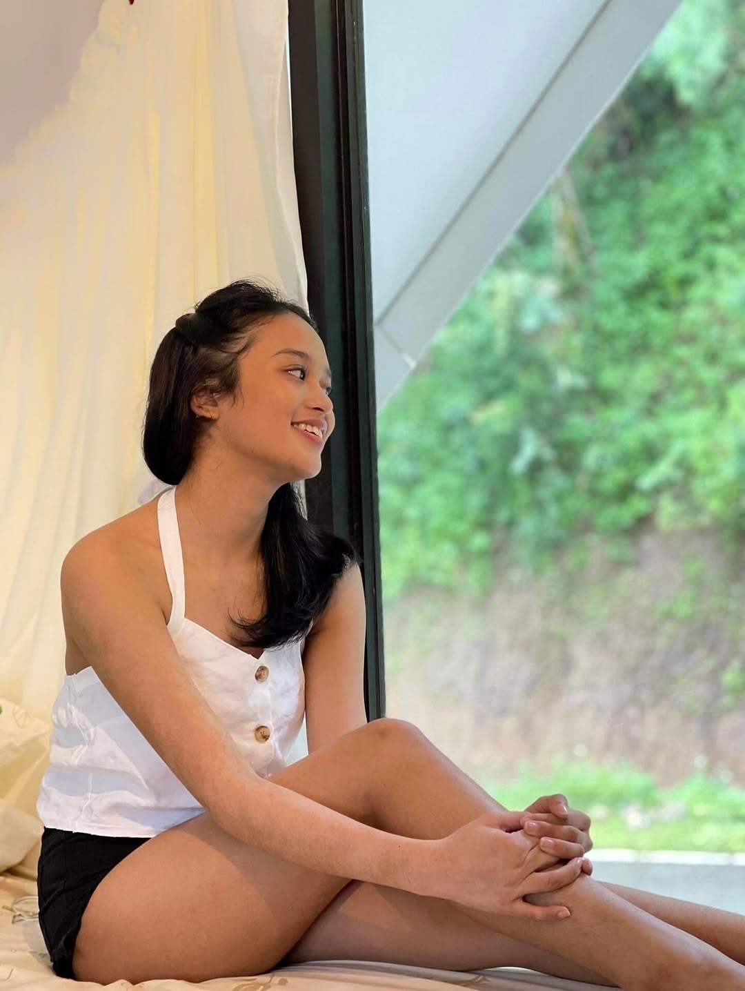 Woman sitting by the large A-frame glass window of the La Cabaña ground floor, smiling at the forest outside